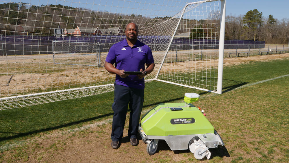 Customer from Darlington schools standing besides the Turf Tank robot with a tablet in his hands