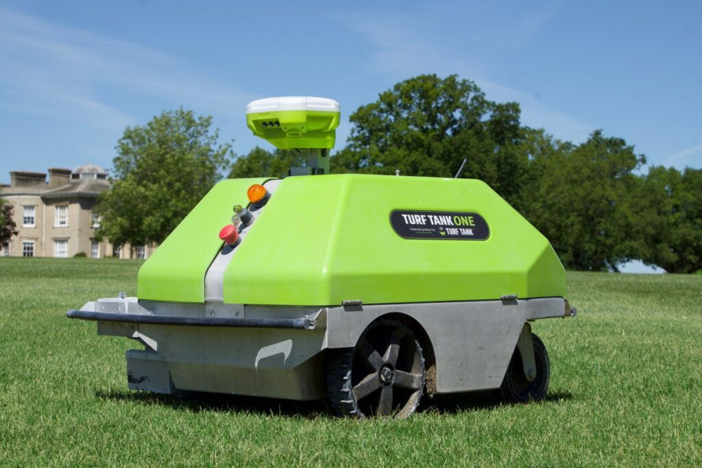 Turf tank robot with standing still for a photo. Gray building in the background