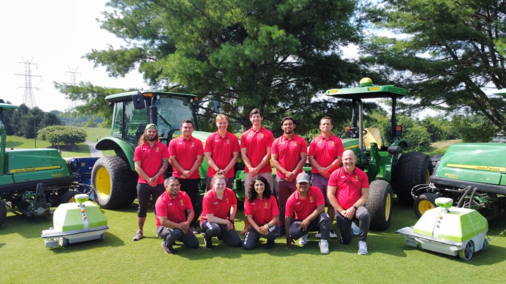 Crew of 11 people posing with two Turf Tank robots and a couple of tractors