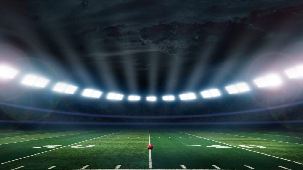 Football field with a ball on the 35 yard line and spotlights lighting down on the ball