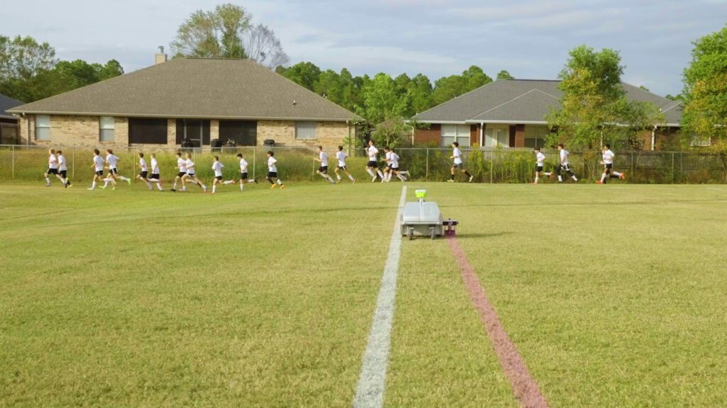 Turf tank robot marking a straight red line while kids are running in front of it