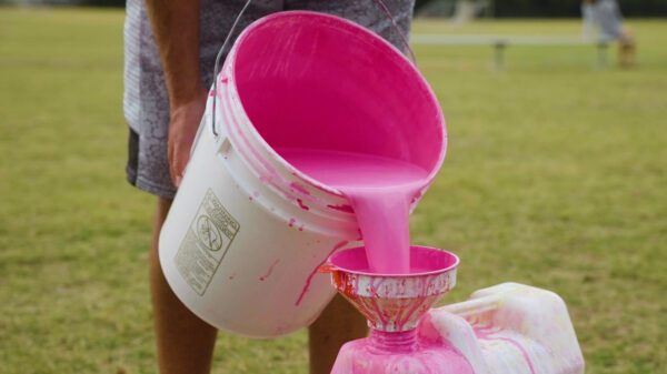 Man filling pink paint inside a 20 liter Turf Tank container