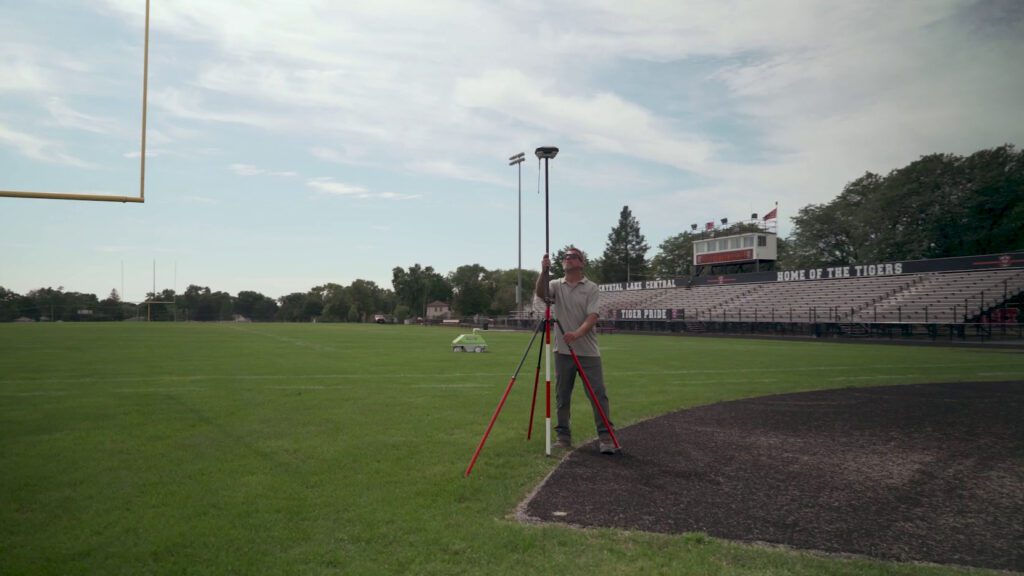 Man setting up tripod and base station next to goal posts on football field
