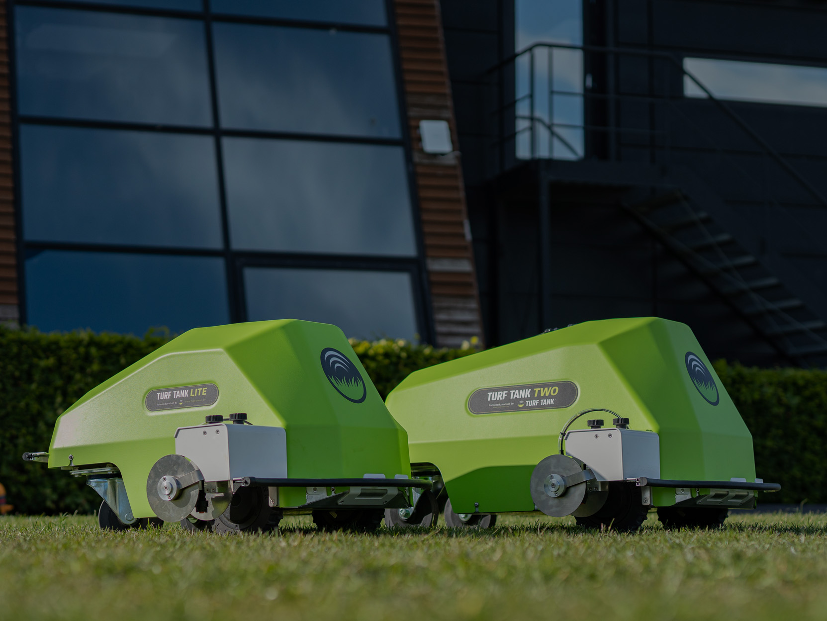 Turf Tank Lite and Turf Tank Two robots lined up in front of the Turf Tank Headquarters