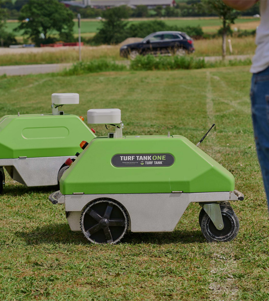 Two Turf Tank one plus robots lined up on a grass field